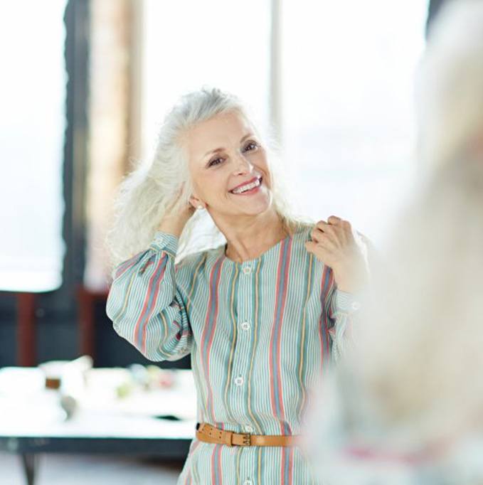 Woman looking in mirror enjoys her dental implant benefits