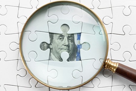 Magnifying glass examining a puzzle with a bill behind an open slot